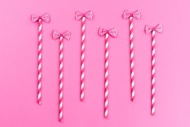 A top view pink-white stick candies with cute bows on pink, sweet sugar color