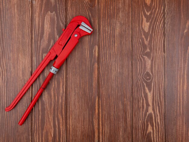 Top view of pipe wrench on left side and wooden background with copy space