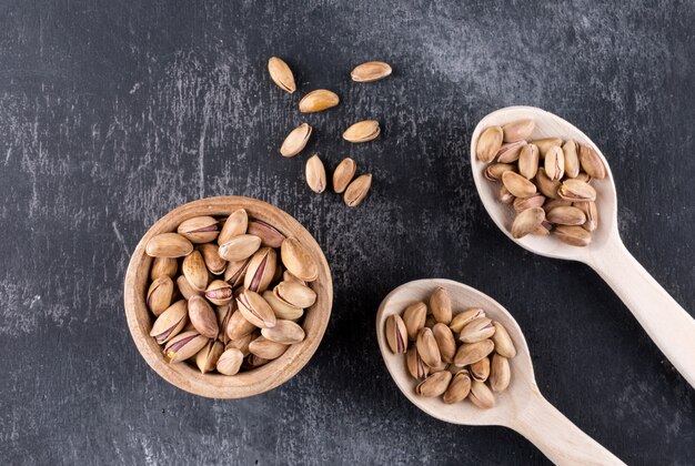 Top view pistachios in a bowl and wooden spoons on gray texture  horizontal