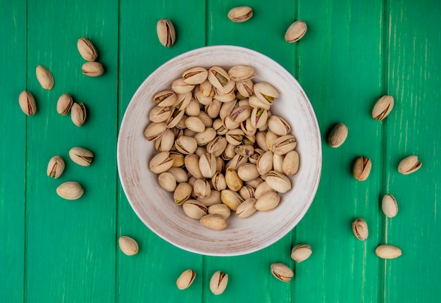 Free photo top view of pistachios in a plate on a green surface