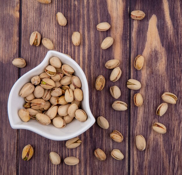 Top view of pistachios in a white bowl on a wooden surface