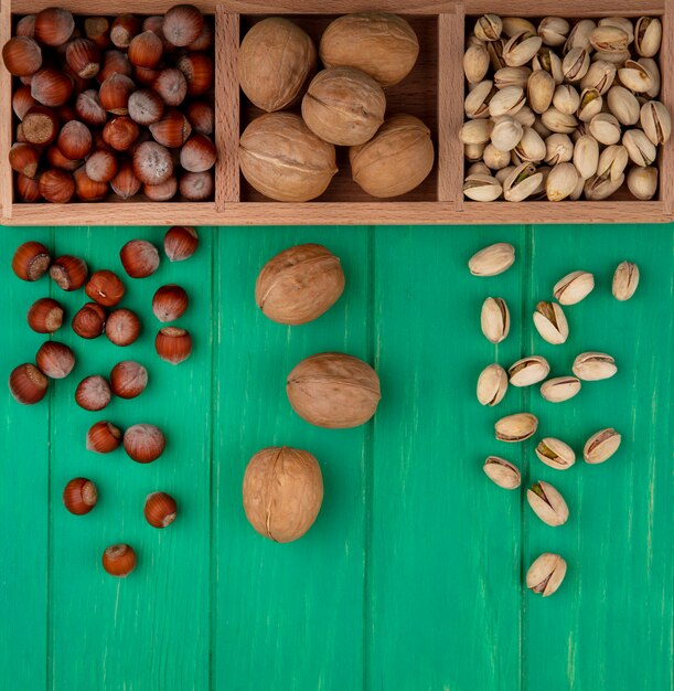 Top view of pistachios with hazelnuts and walnuts on a wooden stand on a green surface