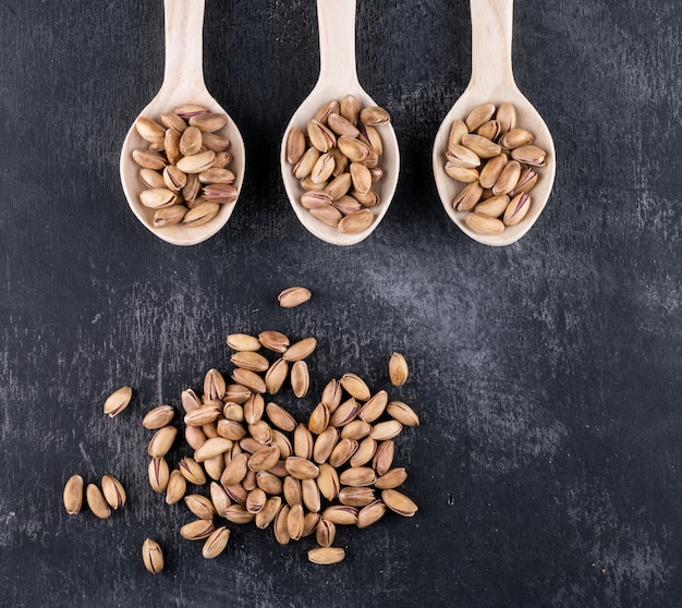 Free photo top view pistachios in wooden spoons on gray texture