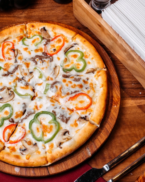 Top view of pizza filled with tomatoes colorful bell peppers salami and olives on a wooden board