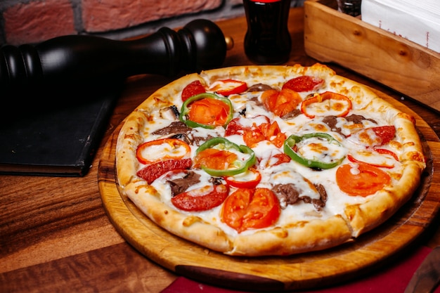 Top view of pizza filled with tomatoes colorful bell peppers salami and olives on a wooden board