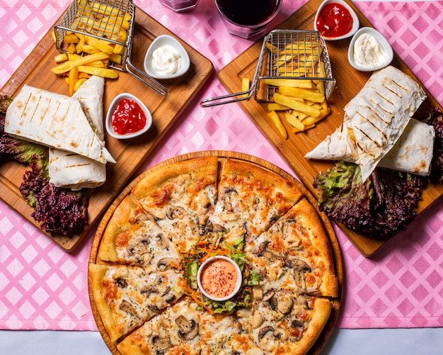 Top view of pizza wirh chicken and mushrooms served with sauce and vegetables salad on a wooden plate