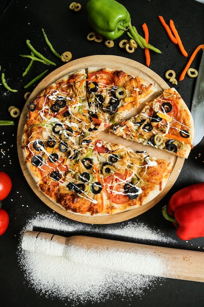 Top view pizza with olives tomatoes bell pepper and rolling pin with flour