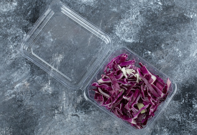 Top view of plastic container full with chopped purple cabbage over grey background. 