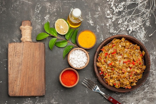 Free photo top view plate of beans and spices bowls of colorful spices lemon the plate of green beans next to the cutting board bottle of oil and fork on the dark table