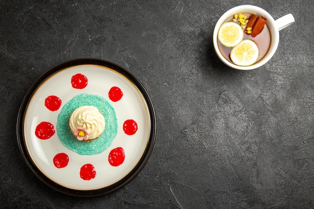 Vista dall'alto piatto di cupcake una tazza di tè con bastoncini di limone e cannella e un piatto di appetitoso cupcake sullo sfondo scuro