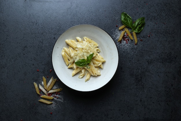 Top view of a plate of pasta with cheese sauce and basil on the black table