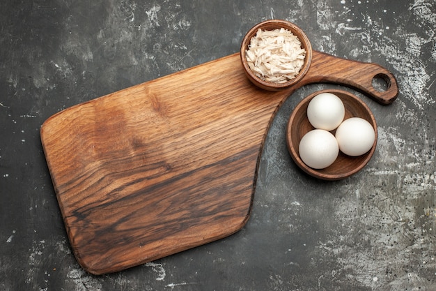 Top view of plate stand with cheese bowl on it and bowl of eggs on side on dark grey table