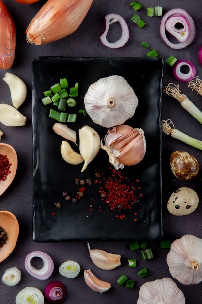 Top view of plate of vegetables as garlic cut scallion with onion egg spices on maroon background