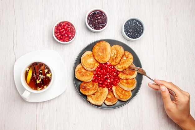 Top view plate on the white table bowls of jam plate of pancakes fork in hand and a cup of herbal tea with lemon on the table