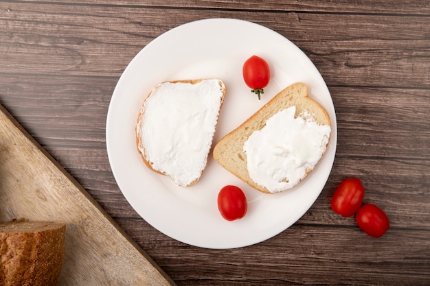 Free photo top view of plate with bread slices smeared with cottage cheese and tomatoes on wooden background