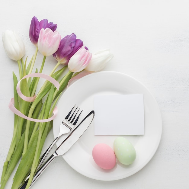 Вид сверху тарелка с пасхальными яйцами и тюльпаны со столовыми приборами
