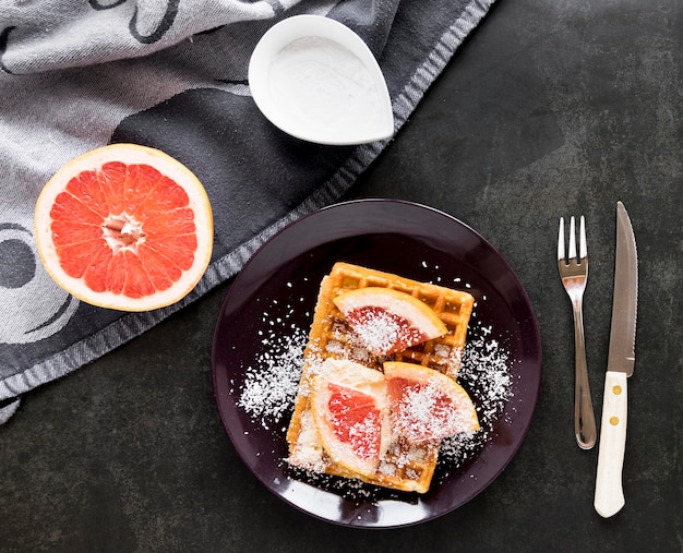 Top view of plate with waffles and citrus dusted with powdered sugar