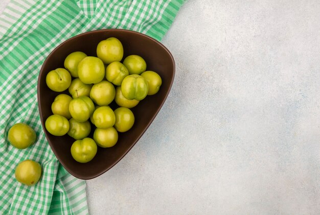 Top view of plums in bowl on plaid cloth on white background with copy space