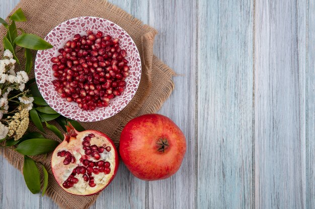 Top view of pomegranate berries in bowl with whole and half ones with flowers on wooden surface