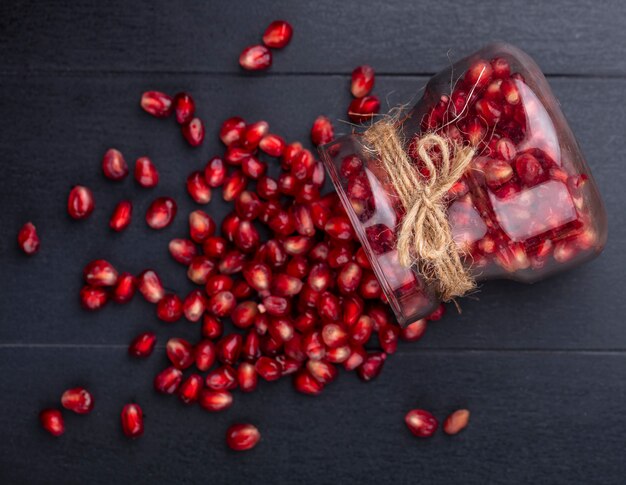 Top view of pomegranate berries spilling out of glass jar on black surface