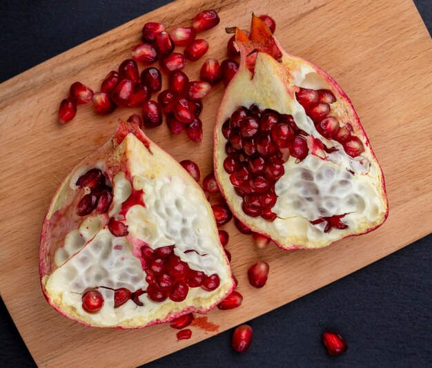 Top view of pomegranate pieces and berries on cutting board on black surface