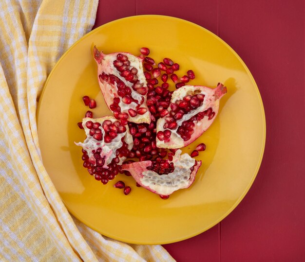 Top view of pomegranate pieces and berries in plate on plaid cloth and bordo surface