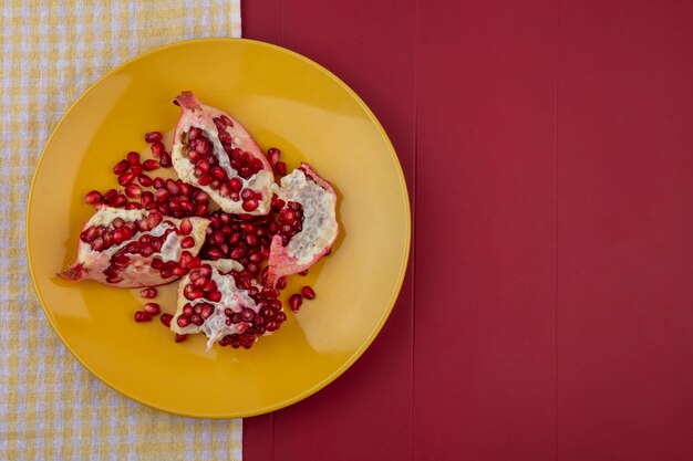 Top view of pomegranate pieces and berries in plate on plaid cloth and bordo surface