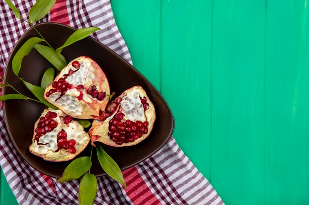 Top view of pomegranate pieces in bowl on plaid cloth and green surface