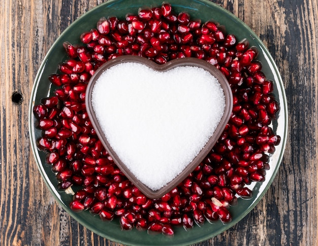 Free photo top view pomegranate in plate with heart shaped plate with sugar on wooden table