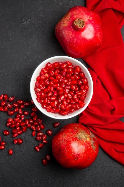 Top view pomegranate pomegranate seeds in the bowl two pomegranates red tablecloth