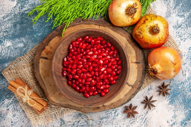 Top view pomegranate seeds in bowl on tree wood board cinnamon anise seeds pomegranates tree branch on blue-white background