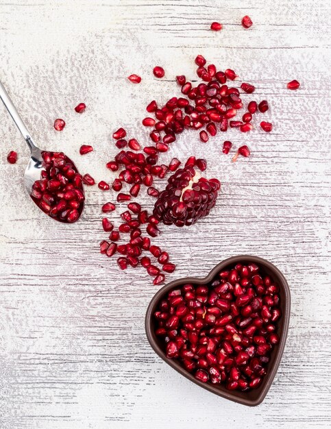 Top view pomegranate seeds in heart shaped plate on white wooden table