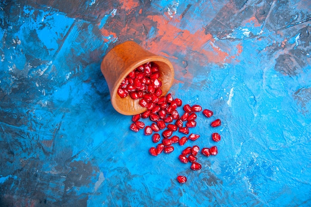 Free photo top view pomegranate seeds in little wooden bowl on blue surface