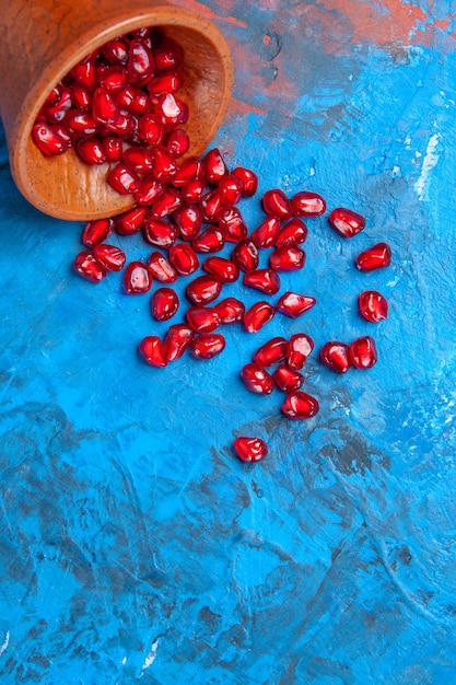 Free photo top view pomegranate seeds in little wooden bowl on blue surface