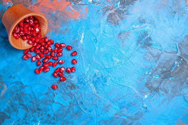 Top view pomegranate seeds in little wooden bowl on blue surface