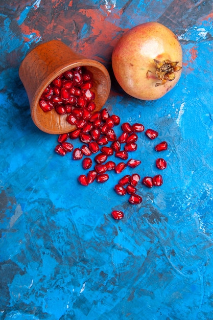 Free photo top view pomegranate seeds in little wooden bowl a pomegranate on blue background with free space