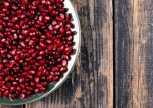 Top view pomegranate seeds in plate with copy space on right on brown wooden  horizontal