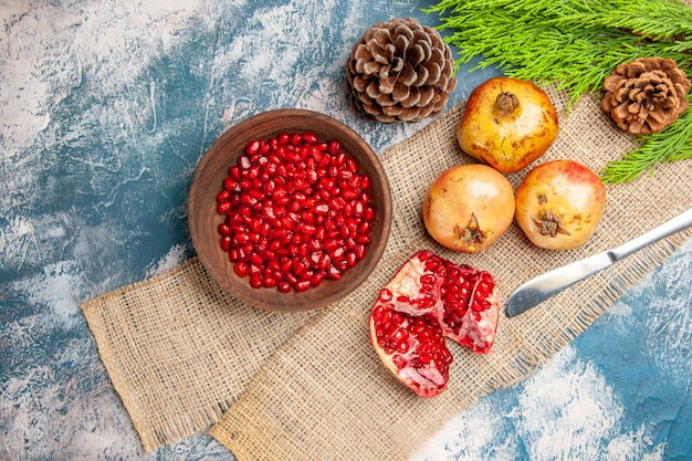 Top view pomegranate seeds in wooden bowl dinner knife pomegranates pine tree branch on blue-white surface
