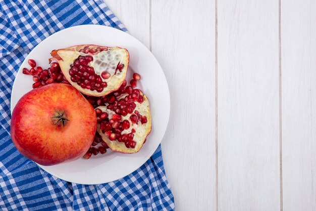 Top view of pomegranate slices on a plate with a blue checkered towel on a white surface