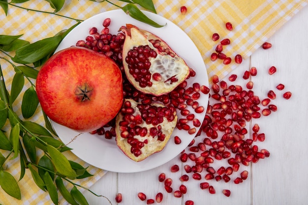 Free photo top view of pomegranate slices on a plate with a yellow checkered towel and leaf twigs
