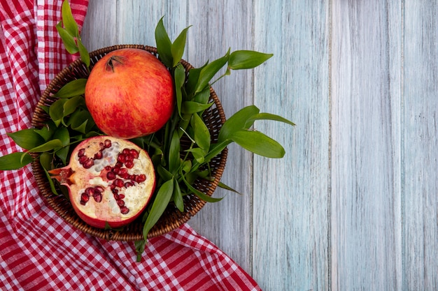 Top view of pomegranate with leaf branches in a basket with a red checkered towel on a gray surface