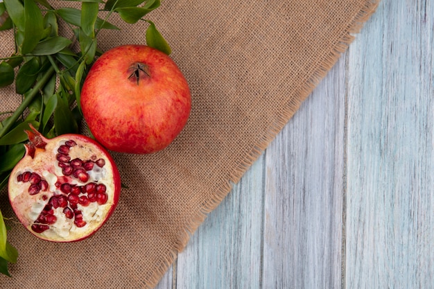 Top view of pomegranate with leaf branches on a beige napkin on a gray surface