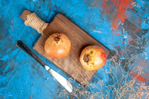 Top view pomegranates on chopping board dinner knife on blue abstract background