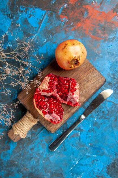 Top view pomegranates on chopping board dinner knife on blue background