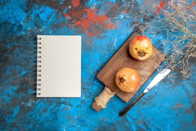 Top view pomegranates on chopping board dinner knife a notebook on blue abstract background