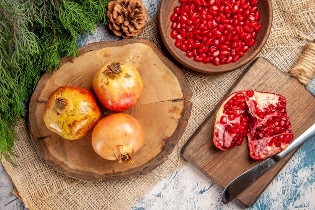 Top view pomegranates on round cutting board pomegranate seeds in bowl a cut pomegranate on chopping board pine tree branch on blue-white background