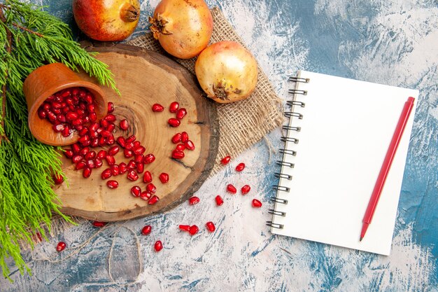 Top view pomegranates scattered pomegranate seeds in bowl on tree wood board a notebook with pen on blue-white surface