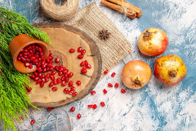 Top view pomegranates scattered pomegranate seeds in bowl on tree wood board straw thread cinnamon anise seeds tree branch on blue-white background