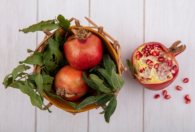 Top view pomegranates with branches of leaves in a basket on a white background