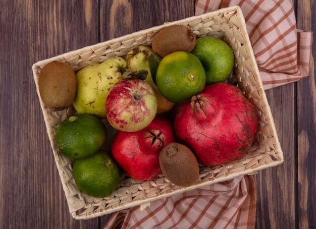 Top view pomegranates with tangerines apples pears and kiwi in a basket on wooden table